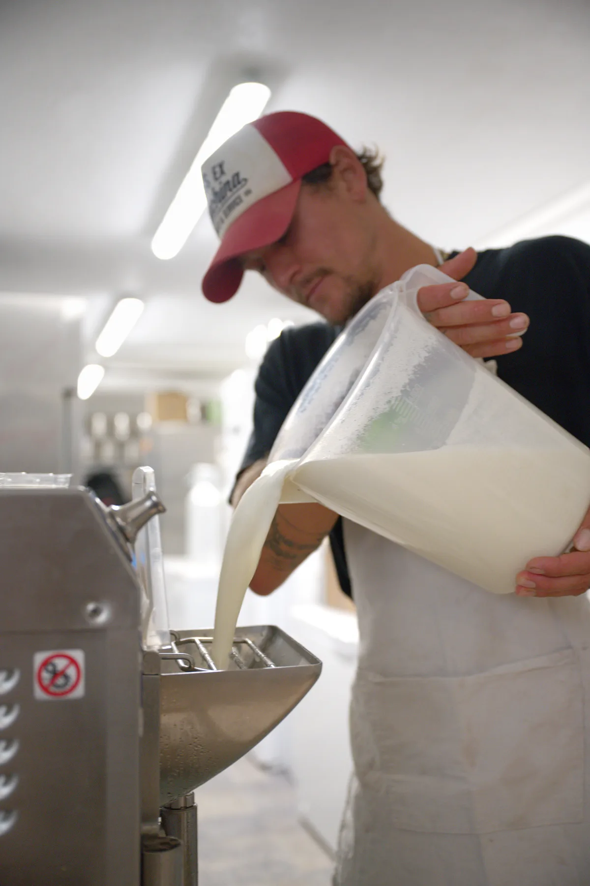 Nach dem Pasteurisieren wird die Milch in die Glacemaschine gegeben. Ein Mann leert Milch in eine Maschine.